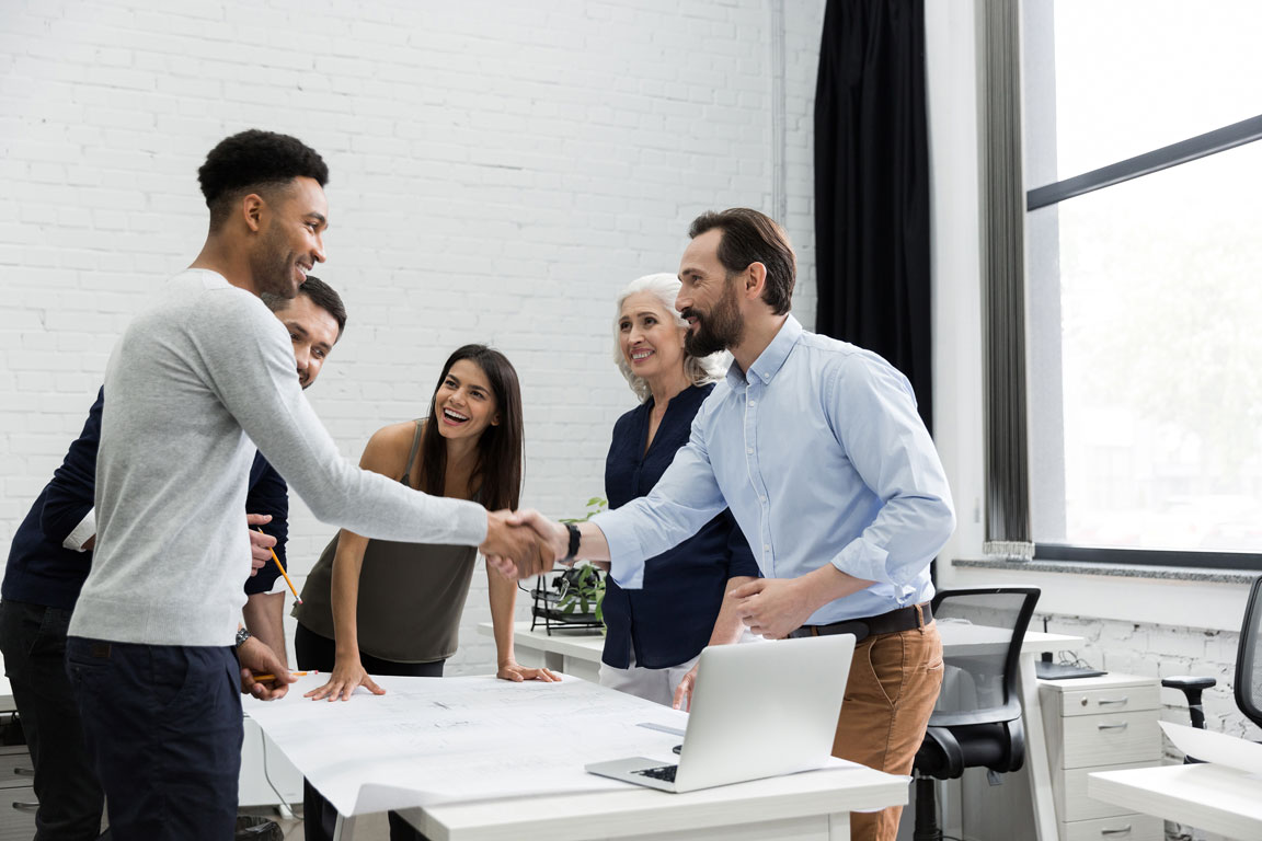 men shaking hands over a table and laptop during business meeting